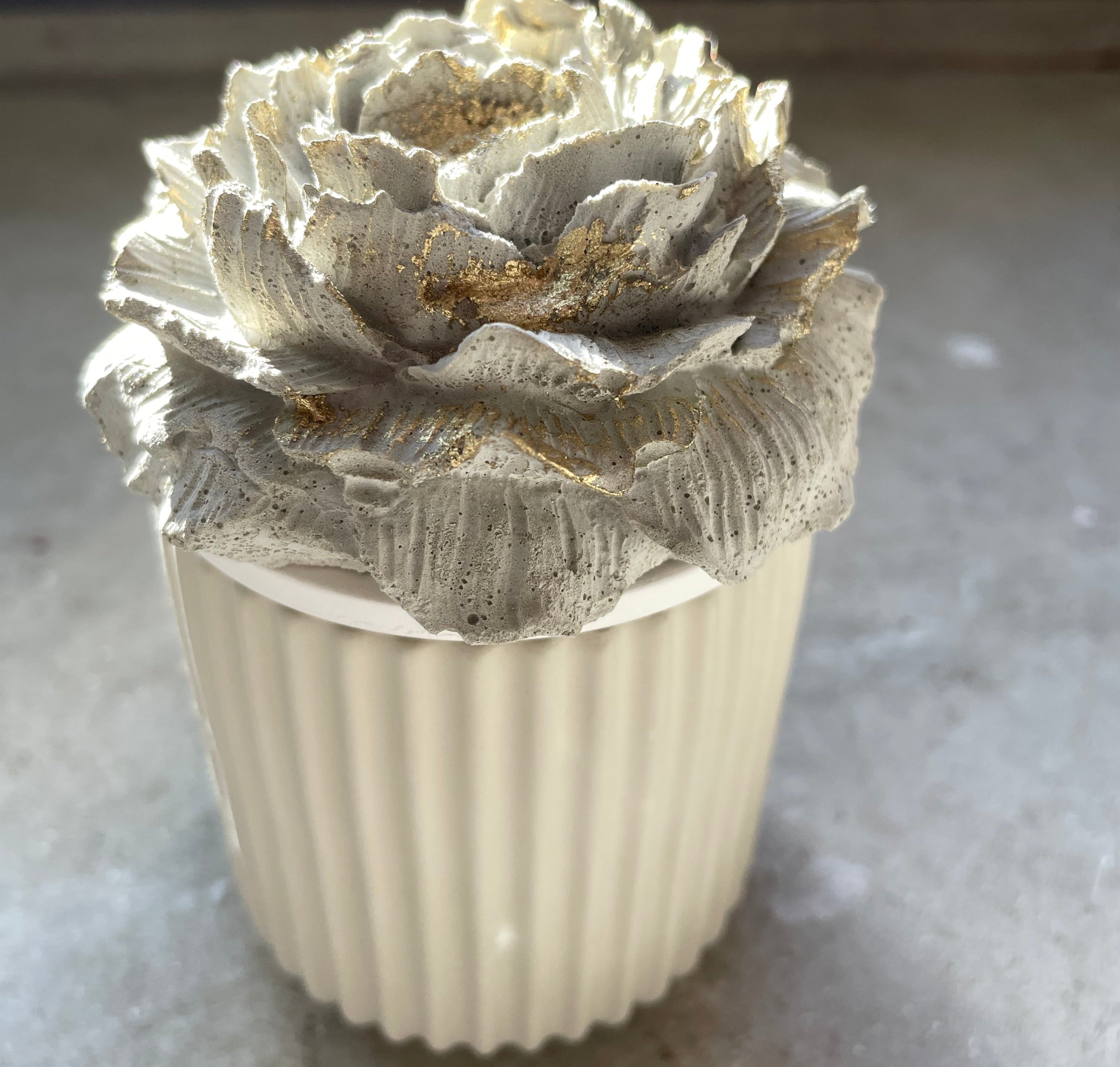 Schmuckdose aus gegossener Keramik mit einer handgegossenen Pfingstrosenblüte aus Beton, filigran modelliert und mit dezenten Goldakzenten veredelt. Die Kombination aus weicher Keramik und rauer Betontextur wirkt modern und künstlerisch. Ideal für Ringe, Ohrringe oder als dekoratives Highlight auf Kommode oder Nachttisch. Ein besonderes Handmade-Objekt für Blumenfans und Liebhaber feiner Details.