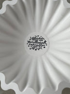 Weiße Keramik-Rillenschale mit 20 cm Durchmesser und zentralem Winterlettering. Die organische Rillenform erzeugt einen modernen Look, perfekt für Kerzen, Zweige oder kleine Winterarrangements. Das Bild zeigt die Schale in einer gemütlichen Winterdeko-Szene mit Naturmaterialien und warmen Lichterketten. Handmade, gegossene Keramik mit seidenmatter Oberfläche und natürlichen kleinen Gießmerkmalen. Ideal für scandi Winterdeko.