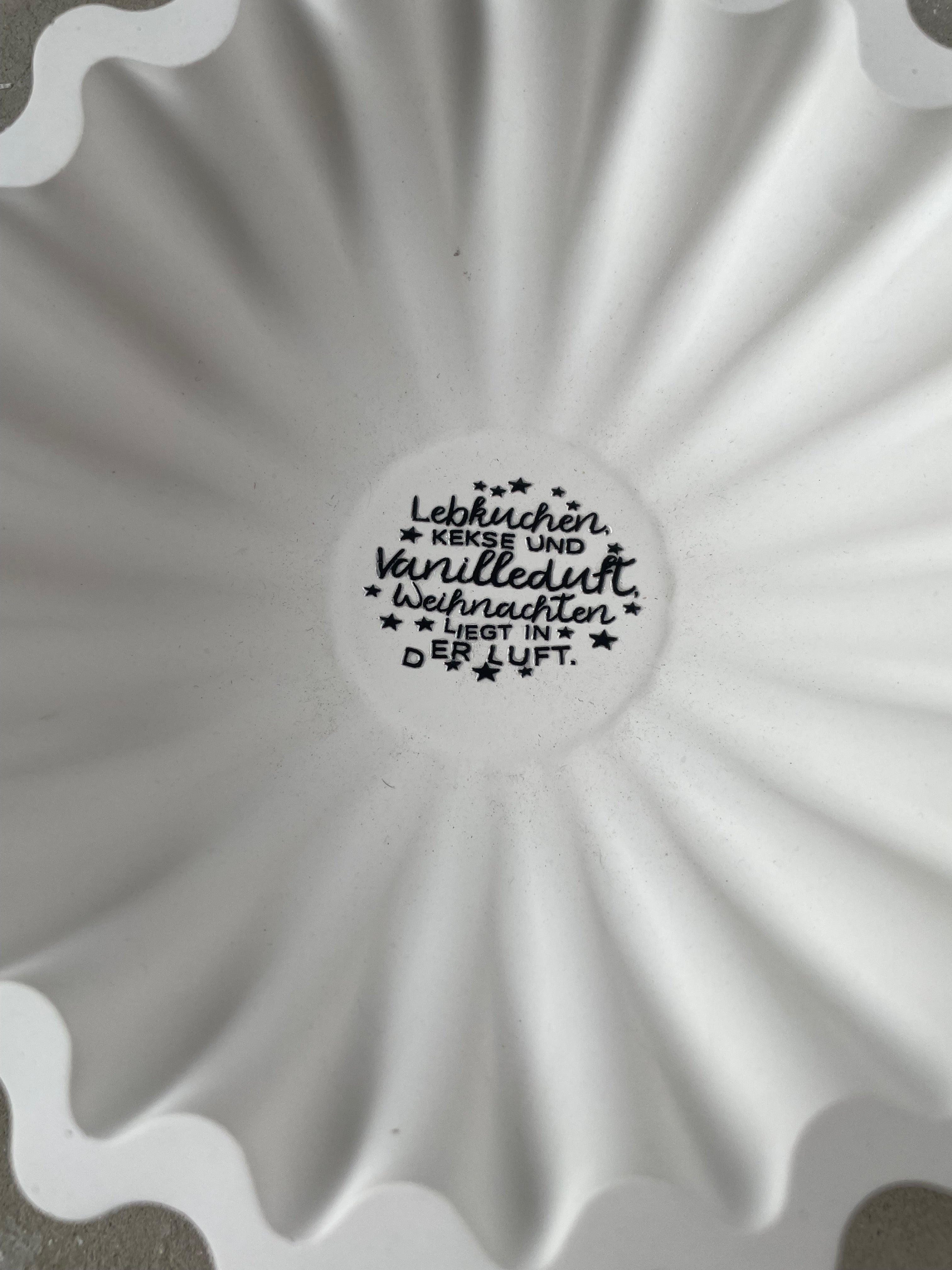 Weiße Keramik-Rillenschale mit 20 cm Durchmesser und zentralem Winterlettering. Die organische Rillenform erzeugt einen modernen Look, perfekt für Kerzen, Zweige oder kleine Winterarrangements. Das Bild zeigt die Schale in einer gemütlichen Winterdeko-Szene mit Naturmaterialien und warmen Lichterketten. Handmade, gegossene Keramik mit seidenmatter Oberfläche und natürlichen kleinen Gießmerkmalen. Ideal für scandi Winterdeko.