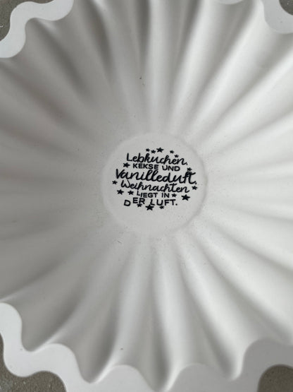 Weiße Keramik-Rillenschale mit 20 cm Durchmesser und zentralem Winterlettering. Die organische Rillenform erzeugt einen modernen Look, perfekt für Kerzen, Zweige oder kleine Winterarrangements. Das Bild zeigt die Schale in einer gemütlichen Winterdeko-Szene mit Naturmaterialien und warmen Lichterketten. Handmade, gegossene Keramik mit seidenmatter Oberfläche und natürlichen kleinen Gießmerkmalen. Ideal für scandi Winterdeko.