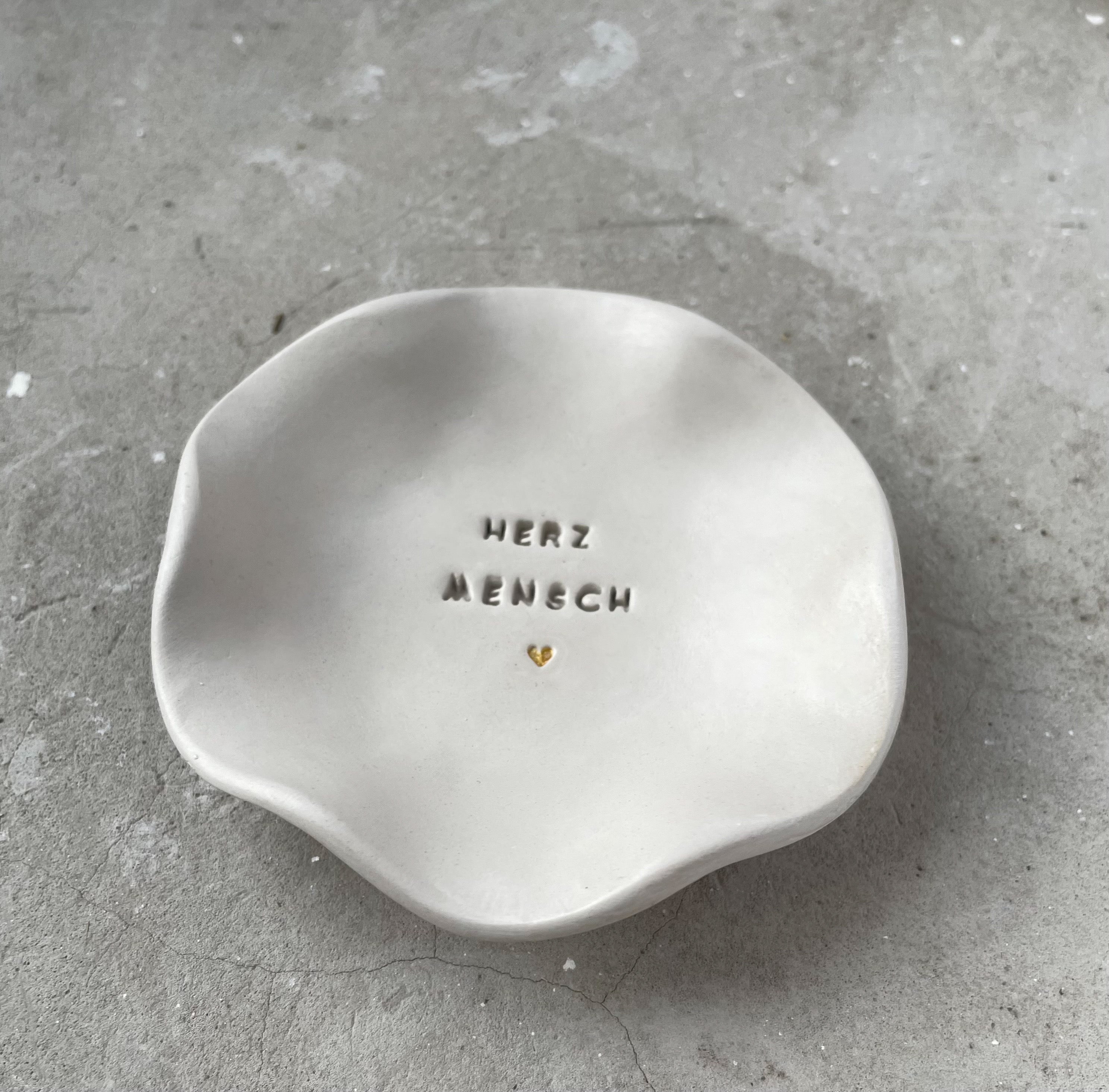 Handgemachte Schale aus hochwertiger weißer Keramikmasse mit dem eingearbeiteten Schriftzug Herzmensch und einem modernen kleinen Herz. Die Schale besticht durch ihre seidenmatte glatte Oberfläche und das minimalistische Design das durch die handgefertigte Prägung eine besonders wertige und persönliche Note erhält. Besonderes Geschenk für Lieblingsmenschen und Mamas