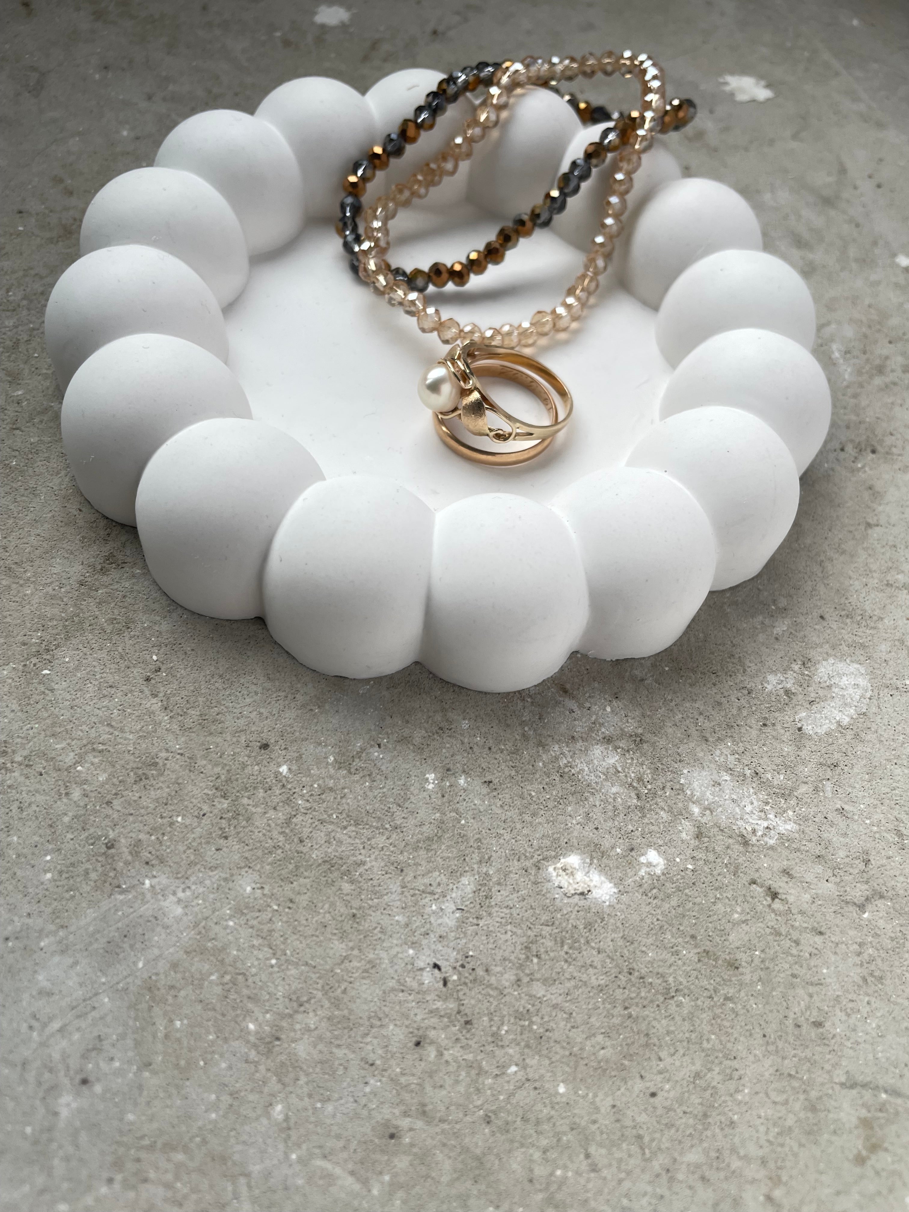 Handgegossene Bubble-Schale aus Keramik mit umlaufenden Kugelrändern. Modern, verspielt und perfekt geeignet für Schmuck, Ringe oder kleine Alltagsstücke. Die sanfte Farbgebung und die weiche Formensprache passen zu modernen, skandinavischen und Boho-Interiors. Die Schale ist stabil, fein geschliffen und langlebig. Ein stilvolles Dekoobjekt und eine süße Geschenkidee für Freundinnen, Interior-Fans und alle, die besondere, handgefertigte Stücke lieben.