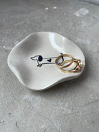 Kleines Dackel-Schälchen aus Keramikguss in Pantone-Beige mit glänzendem High-Gloss-Finish. Ideal als Ablage für Schmuck, Schlüssel oder kleine Alltagsdinge. Innen ein süßes Dackelmotiv mit Herz – perfekt für Hundeliebhaber, Tierfreunde und Fans von minimalistischer, moderner Dekoration. Jedes Stück wird einzeln gegossen, geschliffen und von Hand veredelt. Schlichte Form, glatte Oberfläche, handmade Charakter. Perfekt als Geschenk oder kleine Aufmerksamkeit.