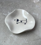 Mini-Schälchen aus Keramikguss in Pantone-Beige, glänzend versiegelt und mit Dackelmotiv. Modernes, schlichtes Design für kleine Dinge wie Schmuck, Haargummis, Münzen oder Schlüssel. Für Hundeliebhaber und Dackelfans eine charmante Dekoidee. Die glatte High-Gloss-Oberfläche wirkt hochwertig und ist leicht zu reinigen. Handmade gefertigt, einzeln gegossen und in kleiner Serie produziert. Perfekt als kleine Geschenkidee, Mitbringsel oder stilvolle Ablage.